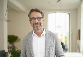Mann mit Brille und grauer Strickjacke lächelt